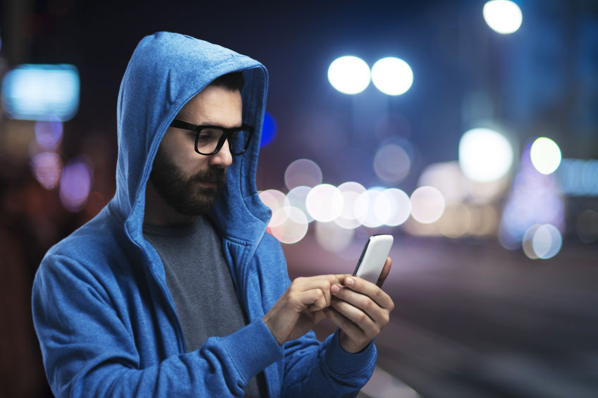 Hombre con capucha en la calle con smartphone